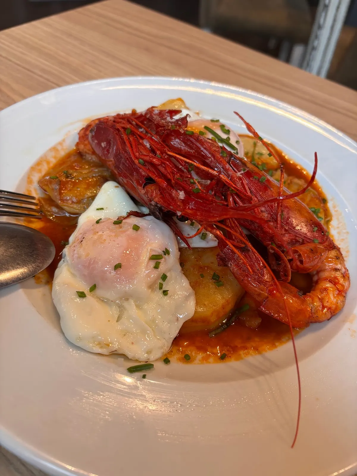 Carabinero sobre patatas panaderas con dos huevos fritos y cebollino, en plato blanco