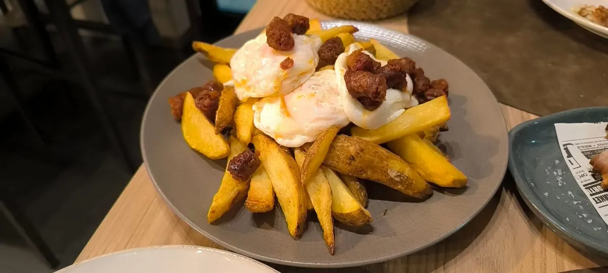 Huevos rotos sobre patatas gajo con trocitos de chistorra