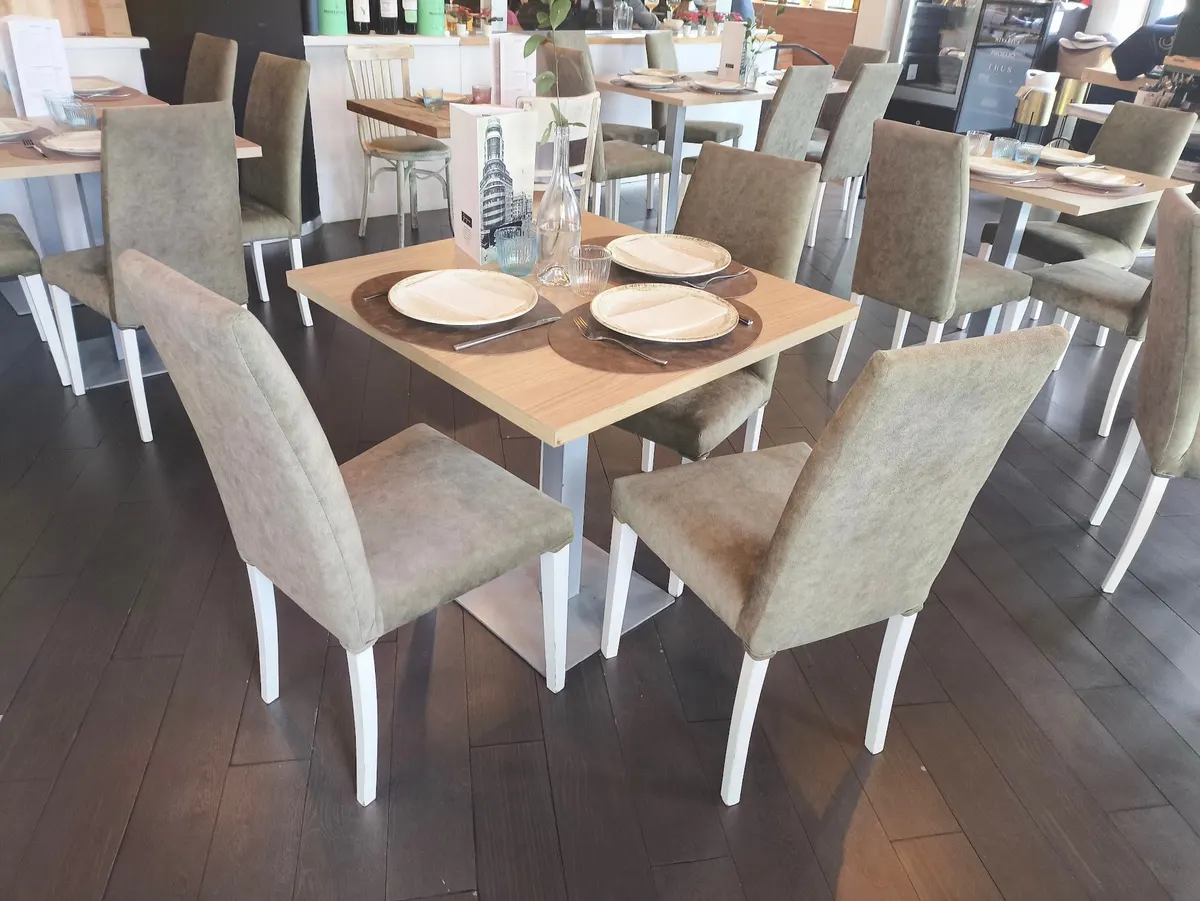 Comedor con mesas de madera clara, sillas tapizadas en verde y la carta sobre la mesa