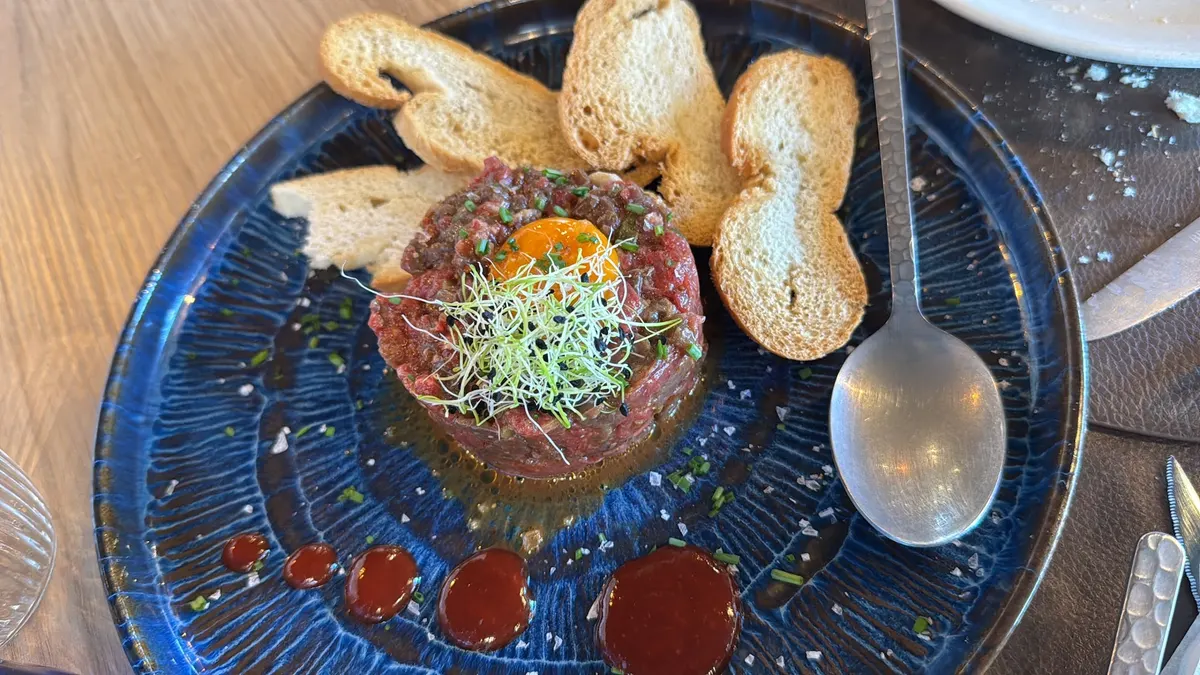 Steak tartar con yema y brotes sobre plato azul, con pan tostado